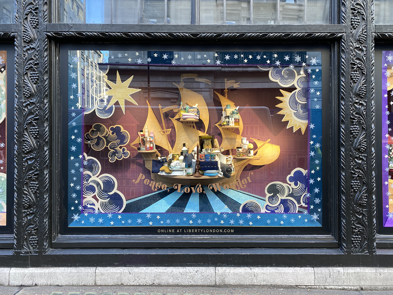 A decorated Christmas window display, with a gold ship, gold writing, and night stars