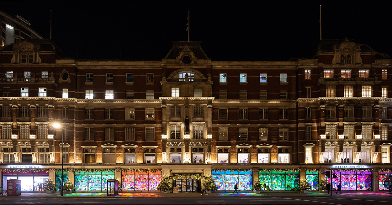 iconic Knightsbridge Harvey Nicols store lit up with their colour stained glass Christmas windows
